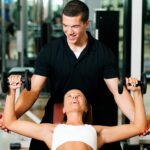 Woman performing a dumbbell press with assistance from a male fitness trainer