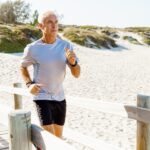 Senior man jogging on a wooden footbridge at a sandy beach on a sunny day