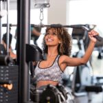 Curly-haired woman performing a lat pulldown exercise at the gym