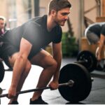 oung man performing a barbell deadlift in an exercise class with other participants